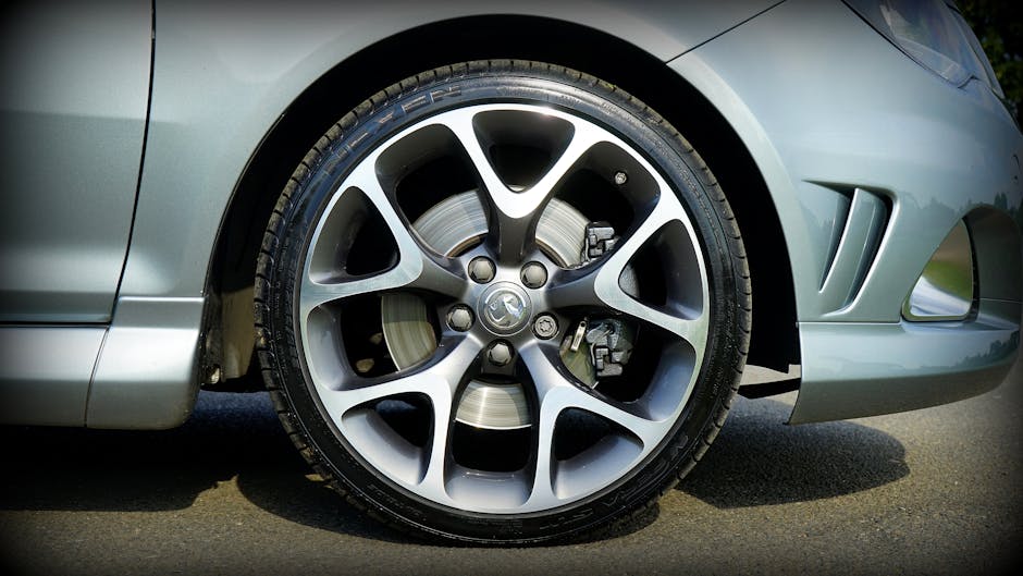 Close-up view of the front wheel of a silver car parked on the street, showing a detailed alloy rim with a five-spoke design and visible brake disc and caliper behind the wheel. The car's bodywork includes a small vent and an integrated side skirt, with the wheel positioned on a paved surface. This image captures part of the vehicle's sleek exterior, highlighting the precision of its tire and alloy wheel assembly, and suggests an outdoor setting with natural lighting. The context aligns with house removals or furniture transport, illustrating the importance of vehicle preparation and loading in the moving process, as seen in professional relocation services like those offered by Man with Van Vauxhall.
